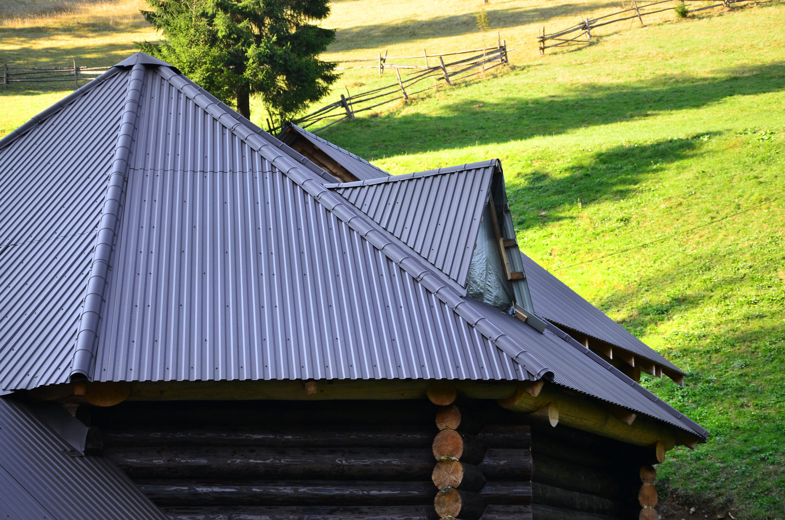 The roof is made of gray embossed metal sheets. Wooden house in the summer field